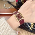 Close-up of a rectangular gold watch with red dial and leather strap on a wrist - Square Roman Numerals