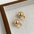 Close-up of gold spherical hoop earrings on a textured wooden display tray - Gold