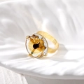 Ethnic gold ring featuring a large amber crystal gemstone on a white fabric background - Adjustable Open / Yellow Round