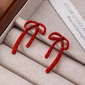 Elegant red bow-knot stud earrings in polished enamel finish for women on wooden display - Red