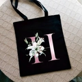 Black canvas tote bag with pink gradient letter H and white lily floral print - Letter H / Black