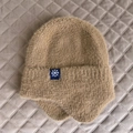 Dettaglio cappello in maglia cammello con paraorecchie, ecopelliccia e fiocco di neve - Taglia unica / Cachi