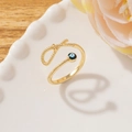 Detail of gold evil eye ring with twisted band on decorative plate and floral background - Style F-Twist Band Eye