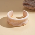 Detailaufnahme des beigen Marmor-Resin-Armreifs auf warmem Sand- und Stein-Hintergrund - Offener Manschetten-Marmorstil / Beige