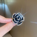 Makroaufnahme eines schwarzen Rosenrings mit diamantbesetzten Blütenblättern am Finger - Brosche mit schwarzer Emaille-Kamelie