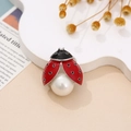 Detalle de broche de mariquita con alas de esmalte rojo y una gran perla central blanca - Estilo Perla
