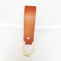 Close-up of brown PU leather keychain with gold metal rivet and ring on white background - Coffee