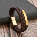 Detail of leather woven bracelet with gold magnetic clasp and metal plaque on dark wood surface - Coffee & Gold