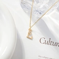 Detailed view of golden letter E necklace with a zircon flower on an elegant magazine background - Letter L