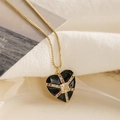 Détail d'un pendentif cœur doré avec émail noir et gemmes colorées sur tissu blanc - Style Croix Cœur Noir Or