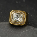 Gros plan d'une bague en acier doré avec zircon rectangulaire sur un socle en pierre - Or + Pierre Blanche / US 7