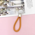 Close-up of a yellow braided leather keychain with silver metal rings on a pink background - Orange