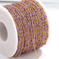 Detailed macro view of golden stainless steel DIY chain with purple enamel beads on a spool - Gold Chain Purple Beads