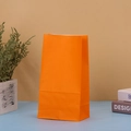 Solid orange kraft paper gift bag for birthday parties and celebrations on a desk - Orange