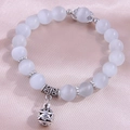 Cat's eye bead bracelet with silver hollow pendant on smooth silk background - White Cat Eye Beads with Silver Hollow Round Ball Pendant