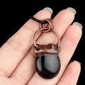 Vintage bronze necklace pendant featuring a smooth black stone, held against black backdrop - Obsidian