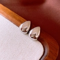 Macro shot of polished silver teardrop earrings reflecting light on a textured background - Silver