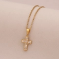 Detalle de un colgante de cruz dorada con circonitas micro-pave sobre un fondo beige texturizado - Jade Blanco