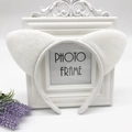 Close-up of white plush cat ear headband displayed on a vintage white photo frame - White Cat Ears