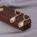 Golden drop earrings with white cat-eye stone and zircon on dark wood display - White Cat's Eye Stone / E-035---Gold