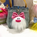 Detailed view of fluffy white monster plush keychain with pink bow on a blue denim bag - White