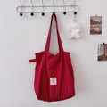 Detail of red striped tote bag with brand label and cute plush sheep charm on a white wall - Burgundy