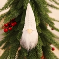 Close-up of a white knitted Christmas gnome hanging on a pine branch with red berries - Knitted Hanging White Style B