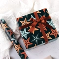 Deep blue gift wrapping paper with orange starfish patterns and a brown satin bow - Star