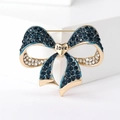 Close-up of golden bow brooch with blue and white crystals and a heart love charm - Blue