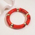 Macro shot of red marble acrylic segments and gold metal beads on a modern bracelet - Red