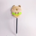 Close-up of cute plush capybara doll topper with green lace on a black ballpoint pen - 0.7mm Bullet Tip / Brown Capybara