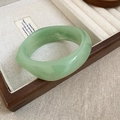 Close-up of thick light green faux jade resin bangle on a wooden jewelry display case - Light Green Jade Pattern