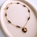 Detailed shot of tiger eye heart pendant with Saturn logo on golden beaded chain - Necklace-Gold-Brown