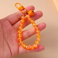 Detail eines orangefarbenen, schimmernden Perlen-Schlüsselanhängers mit kleiner Glocke - Orange