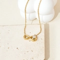 Détail d'un collier pendentif infini doré avec zircon sur une surface en travertin - Or Infini avec Zircone Carré