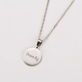 Detalle de cerca de un collar de metal plateado con un colgante circular grabado Dream Big - Color Acero Dream Big