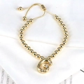 Detail of gold beaded bracelet with zircon-studded letter G charm on white paper - Letter G