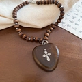Détail de perles en bois sombre et pendentif coeur avec croix en métal sur lin - Café-Croix