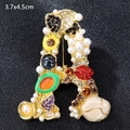 Vintage gold A-letter brooch with colorful gems and pearls on a black display base - Letter A