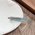 Close-up of a rectangular silver metal hair clip with light blue rhinestones on a tray - Rectangle / Green