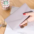 Portafoglio a busta grigio lungo con ciondolo a cuore e nappa tenuto a mano su una scrivania - Viola Chiaro