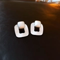 Macro detail of silver square earrings with textured finish on dark leather surface - Silver