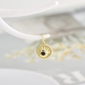Detail of golden sun evil eye pendant with black zircon stone on white jewelry stand - Black Zirconia