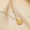 Detail of gold Sagittarius coin pendant on beaded chain over soft beige fabric - Aquarius