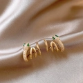 Macro detail of gold snake-shaped earrings with green gemstone eyes and clear zircons - Spiral Snake Style / Gold
