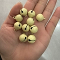 Hand holding ten 14mm pale yellow metal bells for DIY crafts and pet collars - Light Yellow