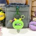 Close-up of fuzzy monster plush keychains with big eyes and colorful letter beads on a bag - Green