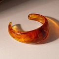 Detail van een amberkleurige hars manchetarmband met schildpadmotief op beige getextureerde stof - Bruin