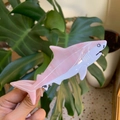 Detailed close-up of a pink and white shark-shaped hair claw clip held over green leaves - Pink Shark White Eye