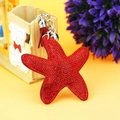 Macro view of a sparkling red starfish keychain with fringe tassel and small metal bell - Red